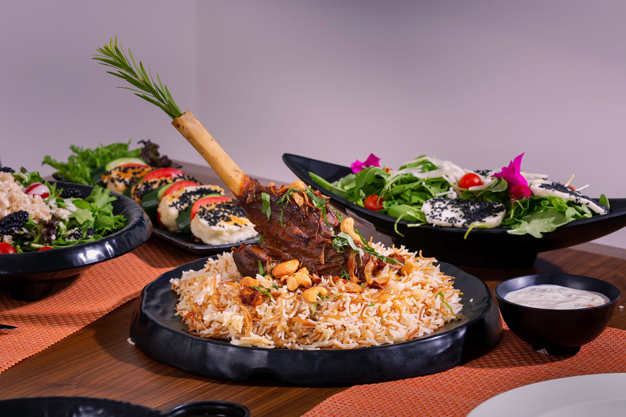 A delicious gourmet lamb shank served with biryani rice and fresh salads on a dining table.