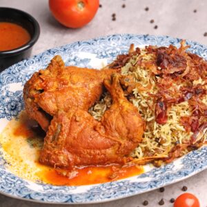 Close-up of flavorful fried chicken served with spiced rice and sauce on a ceramic plate.